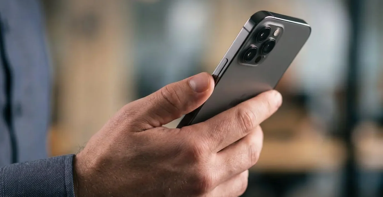 Gros plan sur une main positionnant un smartphone pour reconnaissance faciale dans un environnement professionnel sécurisé